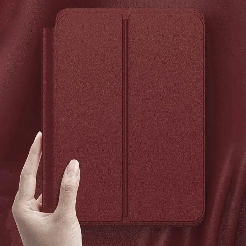 Hand holding a burgundy leather tablet case against matching leather background